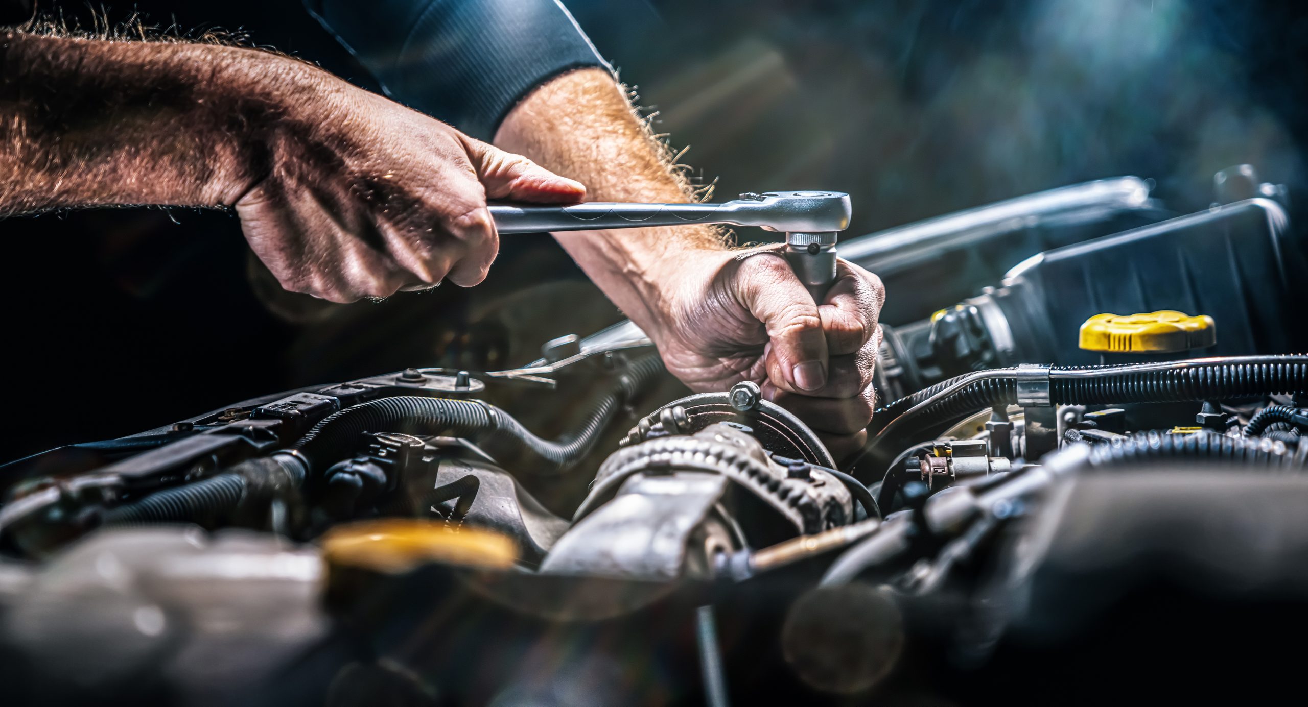Mechaniker benutzt einen Schraubenschlüssel, um an einem Auto-Motor zu arbeiten.