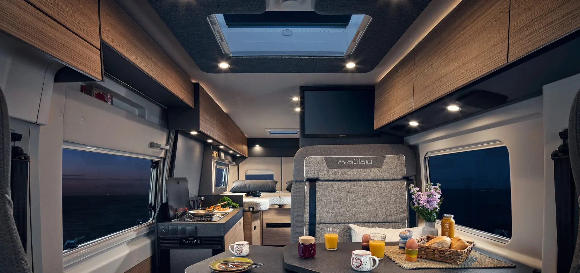 Innenraum eines Wohnmobils mit Holzverkleidung, Tisch und verschiedenen Getränken und Snacks.