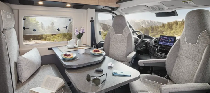 Innenansicht eines Wohnmobils mit einem Tisch, zwei Sitzen und einer Fensteransicht auf die Berge.