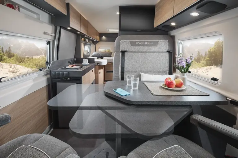 Ein Wohnraumtisch im Malibu Relax Van mit zwei Stühlen und Obst auf dem Tisch.