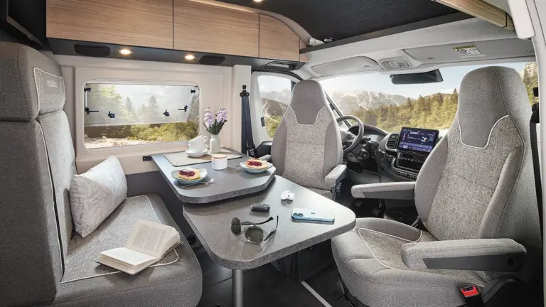 Innenansicht eines Wohnmobils mit einem Tisch und zwei Sitzen, dekoriert mit Geschirr und einer Blume.