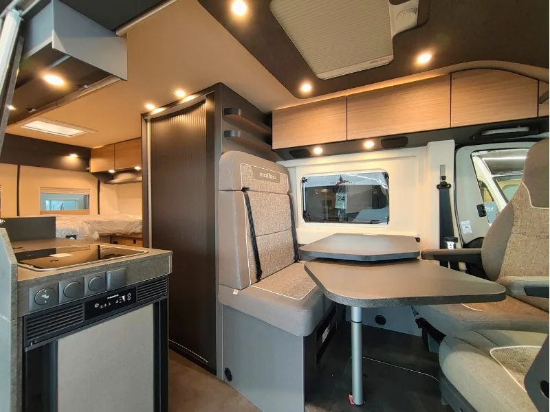 Innenraum eines modernen Wohnmobils mit einem Tisch und zwei Stühlen in neutralen Farben.